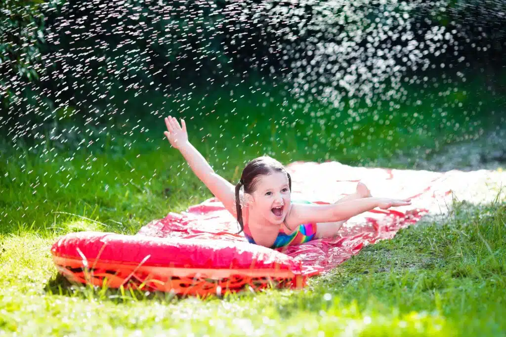 a girl lying on a red water slide in the grass